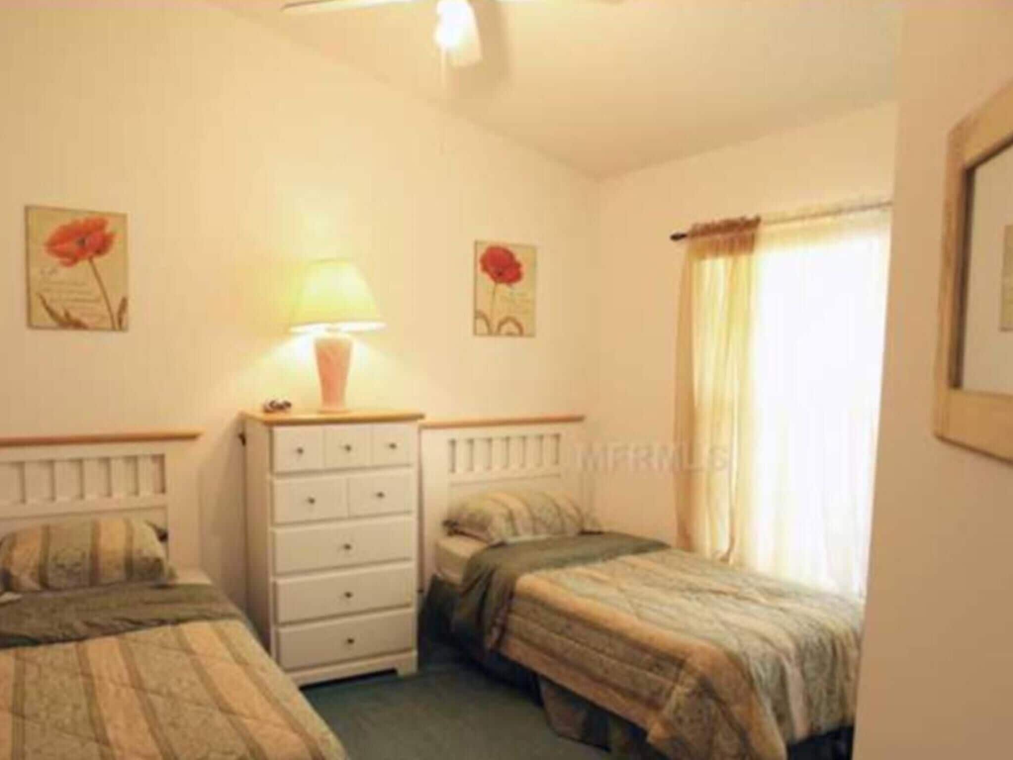 A bedroom with two beds, a nightstand with a lamp, and artwork on the walls.