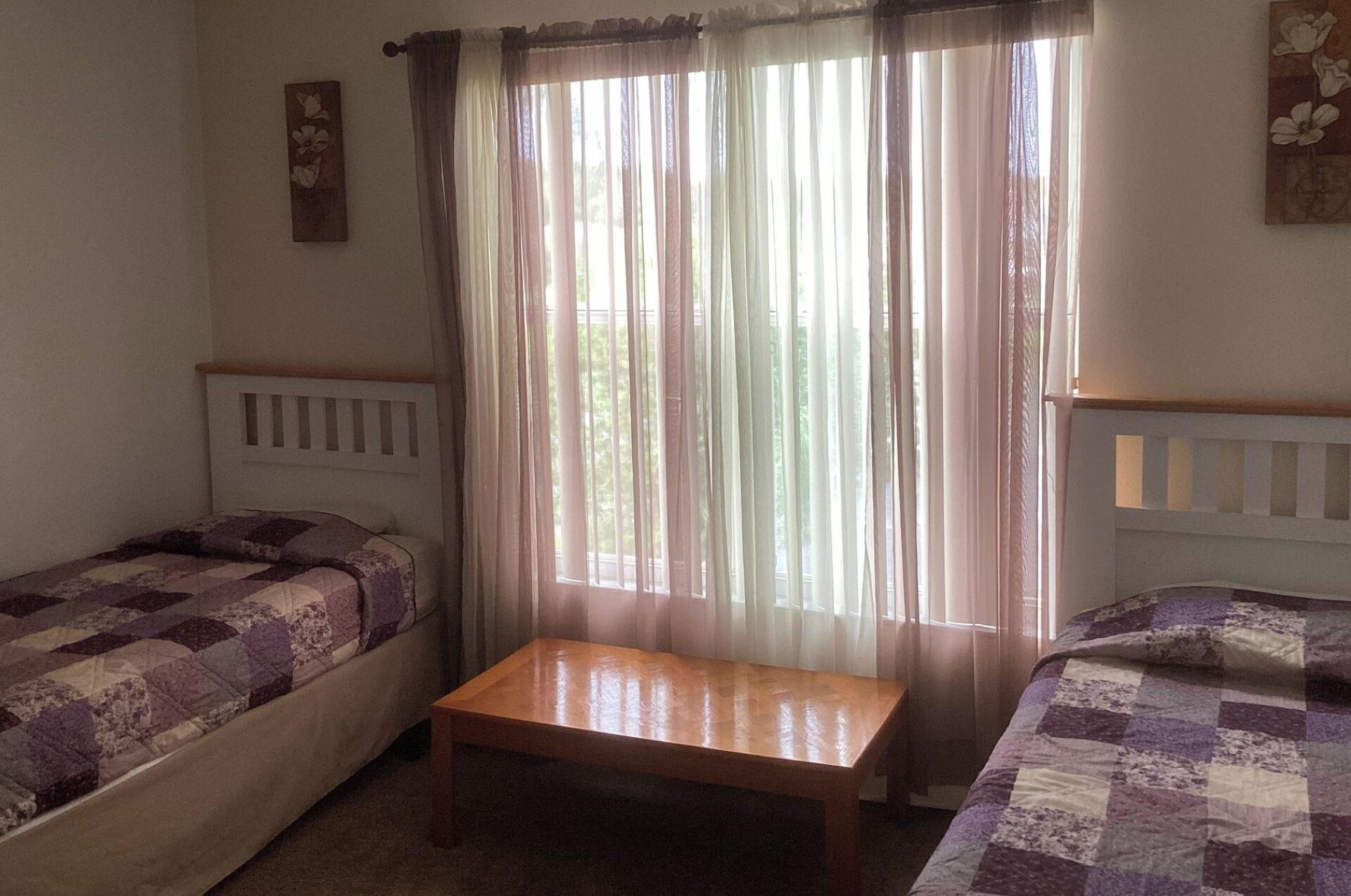 Ein Zimmer mit zwei Einzelbetten, einem Holztisch und transparenten Vorhängen.