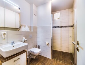 A modern bathroom with a white sink, toilet, and shower area. - Luxuriose Ferienwohnung am Stormthaler See (Grossposna)