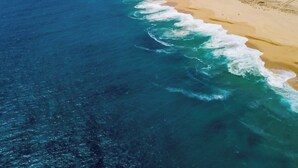 Vista aérea de una playa con aguas azules cristalinas, una orilla arenosa y una montaña al fondo.