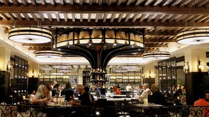 Un restaurante con barra, vigas de madera en el techo y lámparas circulares colgantes.