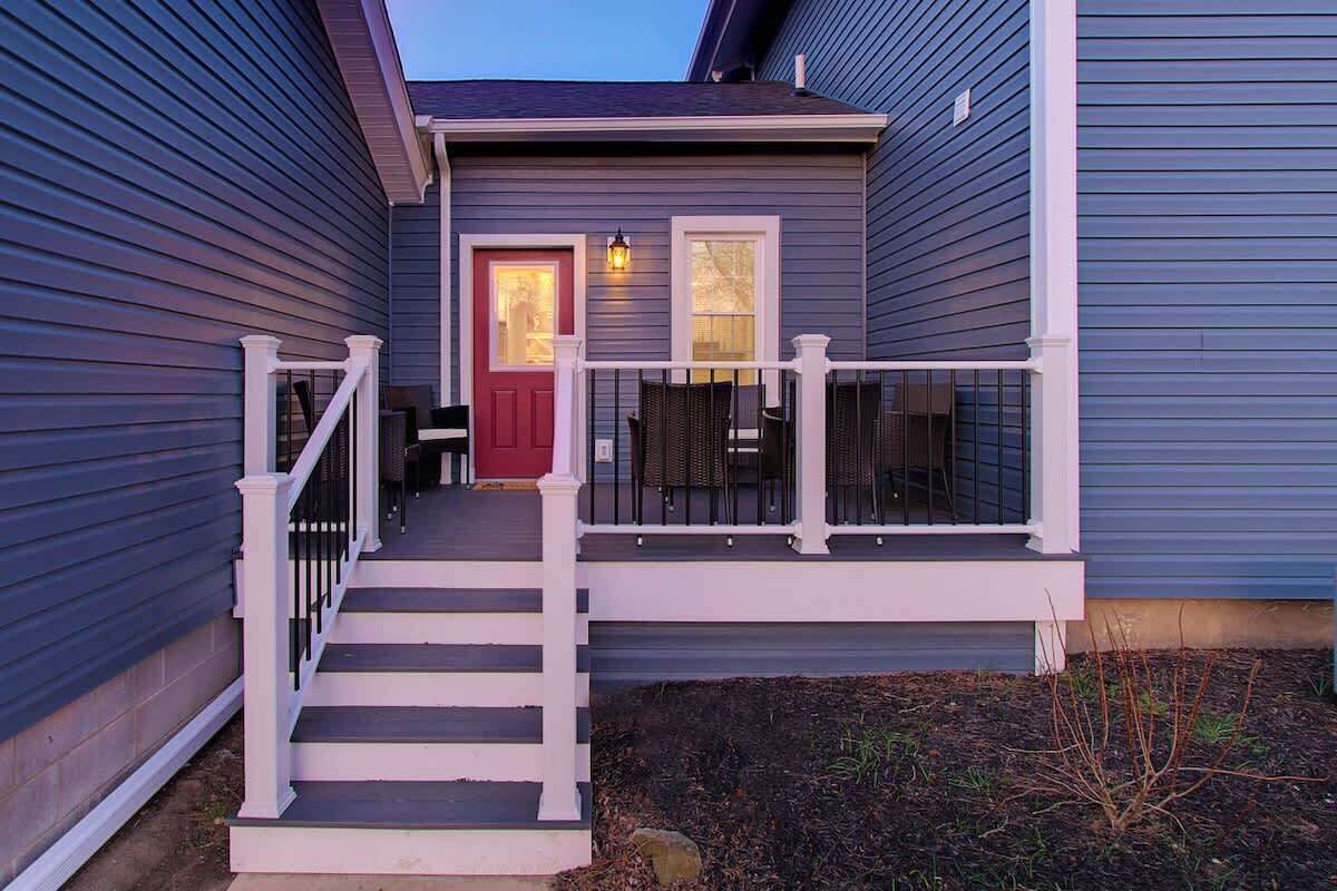 A two-story house with a front porch, a red door, and a small outdoor seating area.