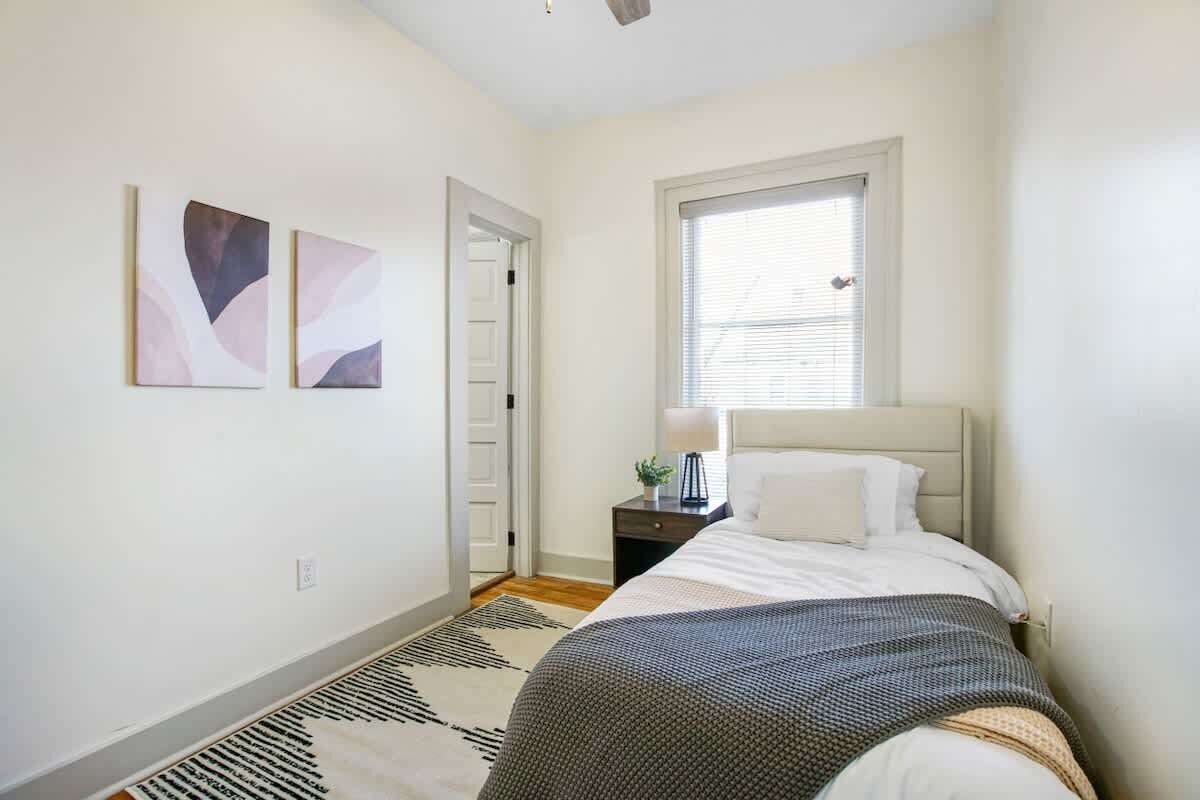 Quarto com cama, mesa de cabeceira, janela e arte abstrata na parede.