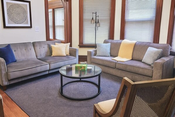 A living room with two grey sofas, a round coffee table, and a wicker chair.