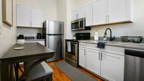 Una cocina compacta con armarios blancos, electrodomésticos de acero inoxidable y un pequeño comedor.