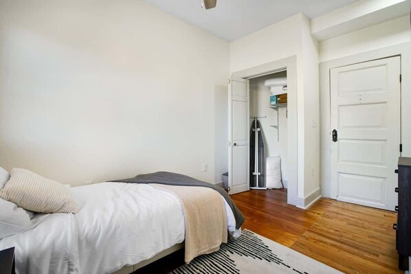 A bedroom with a bed, a door, and a hallway leading to a bathroom.