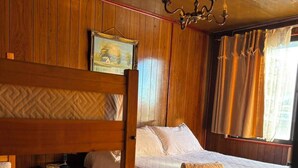 Una habitación con dos literas de madera, una mesita de noche, una lámpara, un cuadro en la pared y una ventana con cortinas.