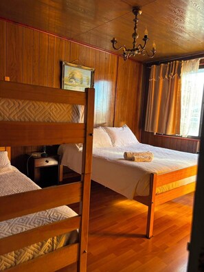 Una habitación con dos literas de madera, una mesita de noche, una lámpara, un cuadro en la pared y una ventana con cortinas.