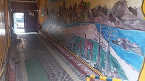 A corridor with a mural depicting a landscape with mountains, trees, and animals. There are yellow and blue poles along the floor, and a green mat.
