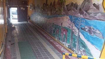 Un pasillo con un mural que representa un paisaje con montañas, árboles y animales. Hay postes amarillos y azules en el suelo, y una alfombra verde.