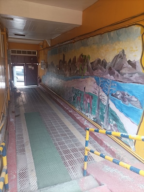 A corridor with a mural depicting a landscape with mountains, trees, and animals. There are yellow and blue poles along the floor, and a green mat.