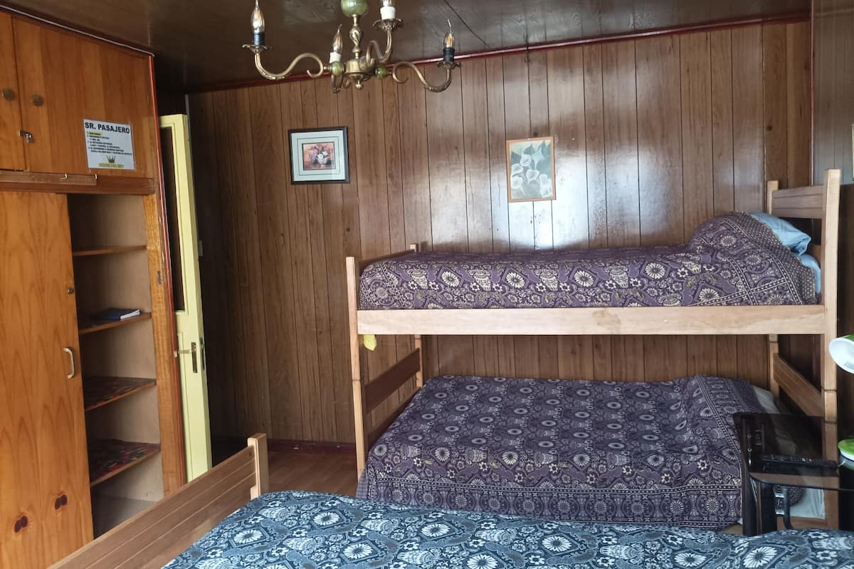 A bunk bed room with wooden walls, a chandelier, and a wooden wardrobe.
