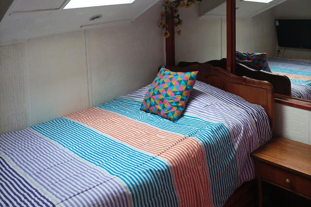 A bedroom with a skylight, a bed with striped bedding, a colorful pillow, and a wooden nightstand.