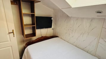 A bedroom with a skylight, a bed, a wooden wardrobe, and a television mounted on the wall.