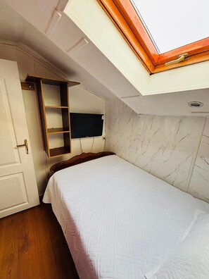 A bedroom with a skylight, a bed, a wooden wardrobe, and a television mounted on the wall. - Alojamiento Familiar del Rey (Punta Arenas)