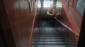 A wooden interior with a staircase leading to a landing area, featuring a potted plant and framed pictures on the walls.