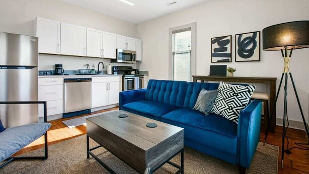 Un apartament modern amb cuina, un sofà blau, una barra de cafè i una làmpada.