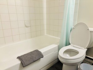 Bathroom features a white bathtub, toilet, and shower area with a light blue shower curtain.