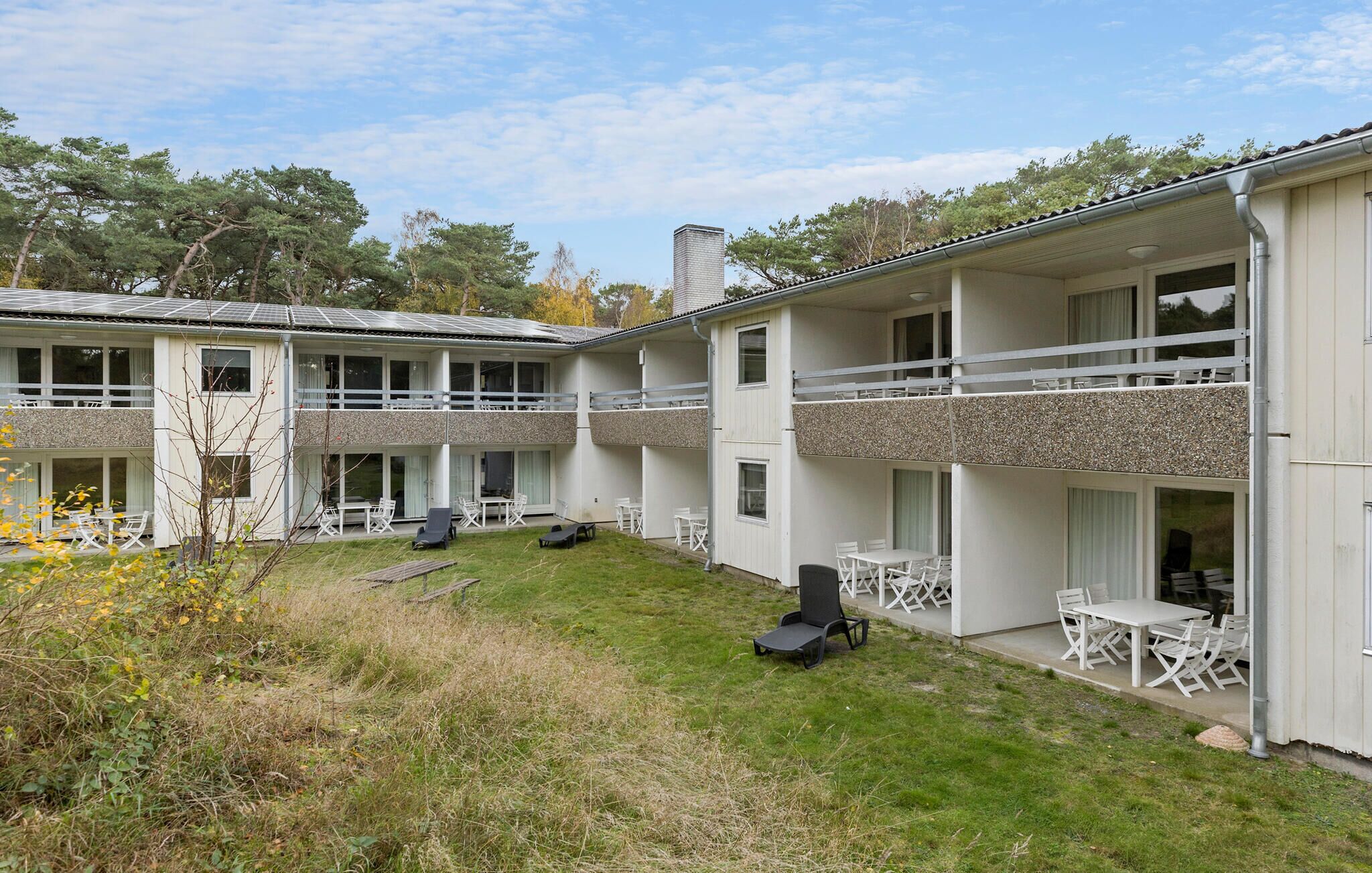A two-story building with a flat roof, outdoor seating area, and a grassy courtyard.