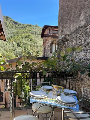 Un espace de restauration en plein air avec une table dressée pour quatre personnes, entouré d’une rambarde en métal, offrant une vue sur une colline verdoyante.