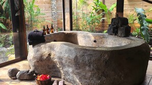 Een stenen hottub met een rustiek design, omringd door een houten omheining en weelderige begroeiing.