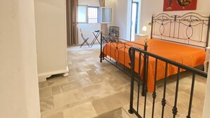 A bedroom with a stone-tiled floor, a bed with an orange bedspread, a metal headboard, and a red abstract painting on the wall. - HOUSE CENTER CASTRIGNANO 3 (CASTRIGNANO DEL CAPO)