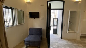A room with a bed, a television, a window, and a door leading to another room. - HOUSE CENTER CASTRIGNANO 2 (CASTRIGNANO DEL CAPO)