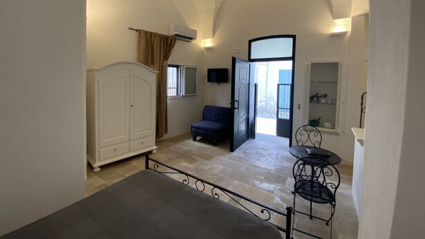 A room with a bed, a wardrobe, a small table, and a chair. There is a door leading to an outdoor area. - HOUSE CENTER CASTRIGNANO 2 (CASTRIGNANO DEL CAPO)
