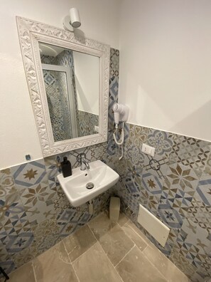 Um banheiro com pia branca, espelho com moldura decorativa, secador de cabelo e azulejos estampados.