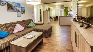 A modern living room with a sofa, coffee table, and a dining area in the background. - Luxuriose Ferienwohnung am Stormthaler See (Grossposna)