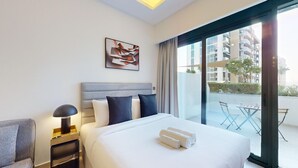 Een hotelkamer met een groot bed, een nachtkastje met een lamp, een schilderij aan de muur, en een balkon met een tafel en stoelen.