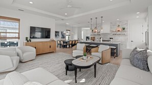 A modern living room with a sofa, coffee table, and TV. There is a kitchen area with a dining table and chairs. - The Golden Palms at St. Augustine Beach (Saint Augustine Beach)
