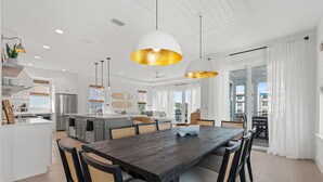 A modern kitchen with a central island, white cabinetry, and stainless steel appliances. There is a dining area with a wooden table and chairs. - The Golden Palms at St. Augustine Beach (Saint Augustine Beach)