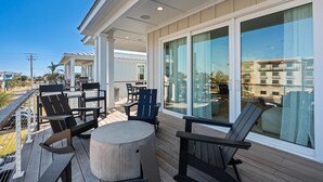 A covered outdoor deck with seating and a table, large windows, and a view of the surrounding buildings. - The Golden Palms at St. Augustine Beach (Saint Augustine Beach)