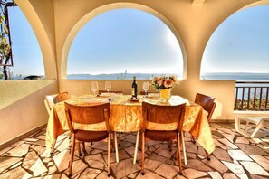 Enjoy meals with a view of the sea from this outdoor dining area, featuring a table for four and comfortable seating.