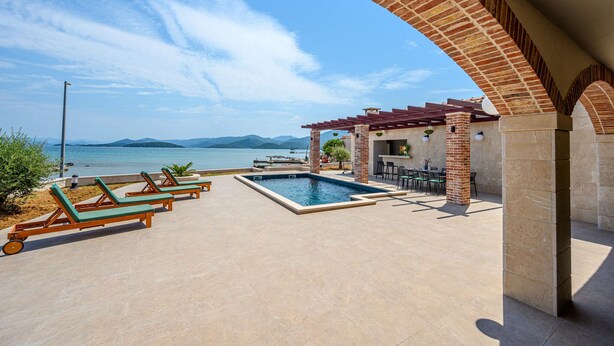 Un área de piscina con sillones de descanso, zona de barbacoa y vista al mar.