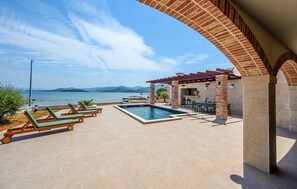 Un área de piscina con sillones de descanso, zona de barbacoa y vista al mar.