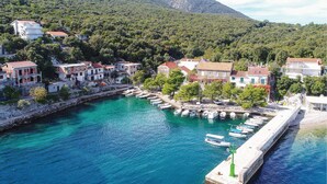 Un pueblo costero con un puerto deportivo, edificios de piedra y montañas al fondo.