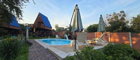 Un patio trasero con piscina, sillas de descanso y una terraza de madera.