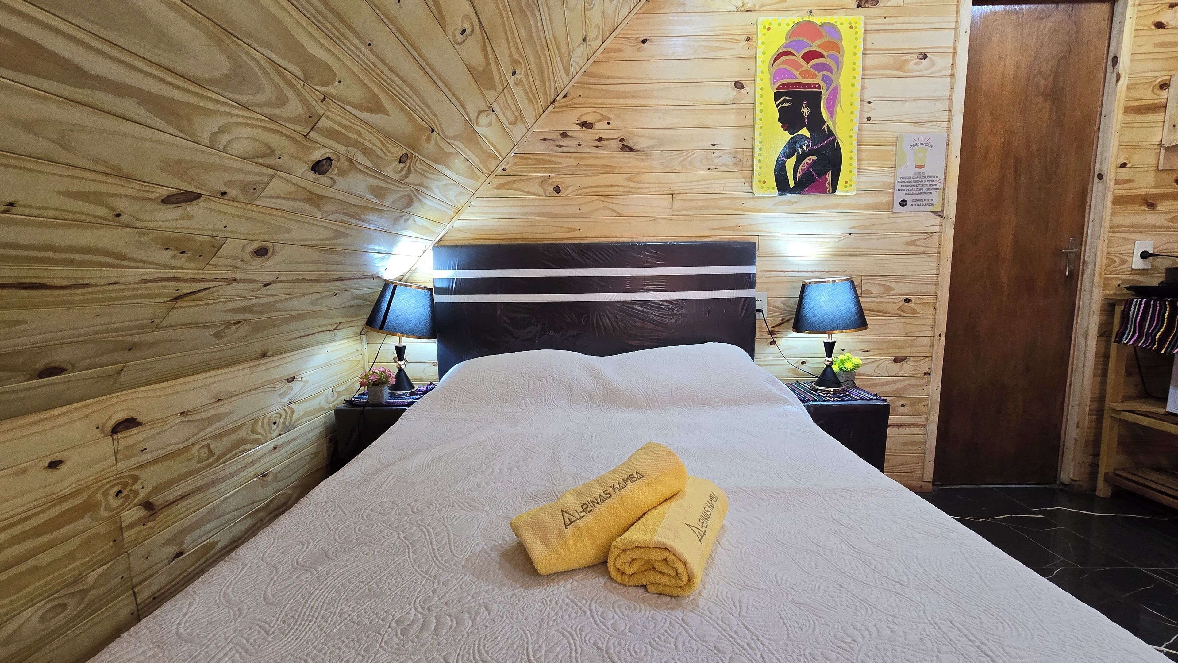 Una habitación con paneles de madera, una cama, dos mesitas de noche con lámparas y un cuadro en la pared.