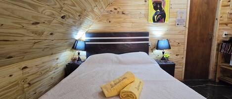 Una habitación con paneles de madera, una cama, dos mesitas de noche con lámparas y un cuadro en la pared.