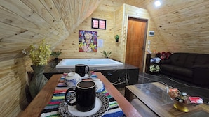 Interior acogedor de una cabaña con paredes y detalles de madera, una bañera, un sofá y una mesa de centro con una taza.