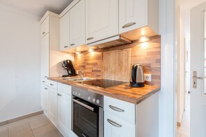 Une cuisine moderne avec des armoires blanches, un plan de travail en bois, un four encastré et une machine à café.