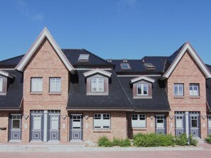 Een rij herenhuisjes van baksteen met puntige daken en dakkapellen.