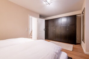 Een slaapkamer met een groot bed, een garderobe en een deur naar een trap.