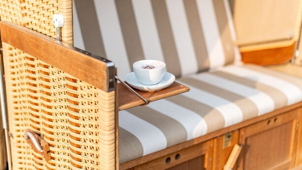 A wicker chair with a striped cushion and a cup of coffee on a tray. - House Nordmarkgarten, Whg. 02a - House Nordmarkgarten (Sylt)