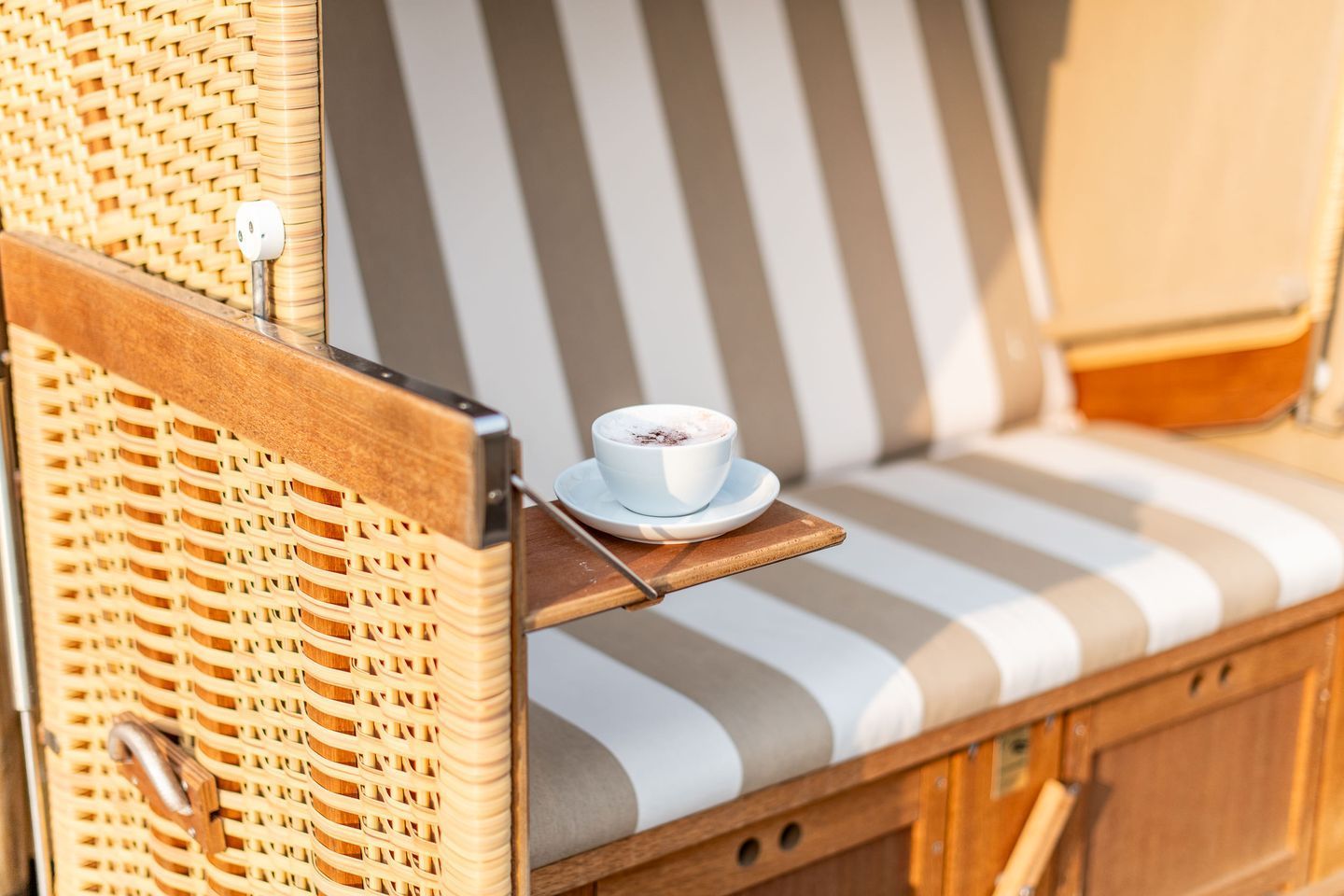 A wicker chair with a striped cushion and a cup of coffee on a tray.