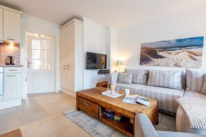 Een moderne woonkamer met een houten salontafel, een bank en een televisie. Aan de muur hangt een schilderij van een strandgezicht.