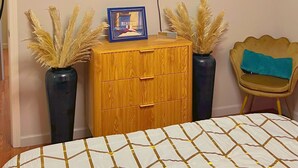 A bedroom with a bed, a TV mounted on the wall, a wooden dresser, and a small shelf with decorative items. - Vibrant Furnished Studio, Walk to LSUNO, 30+ Day Stays (New Orleans)
