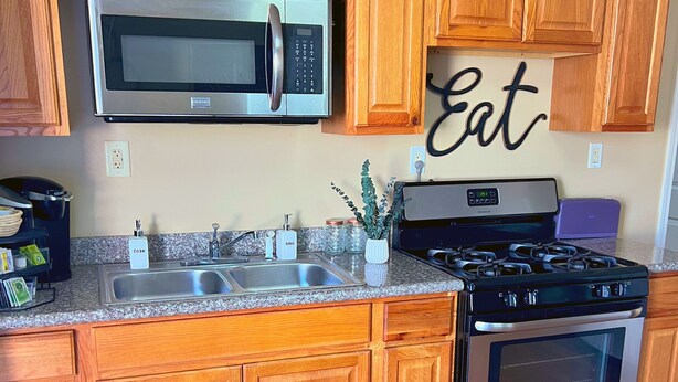A kitchen with wooden cabinets, a stainless steel microwave, a stove, and a sink. - Vibrant Furnished Studio, Walk to LSUNO, 30+ Day Stays (New Orleans)